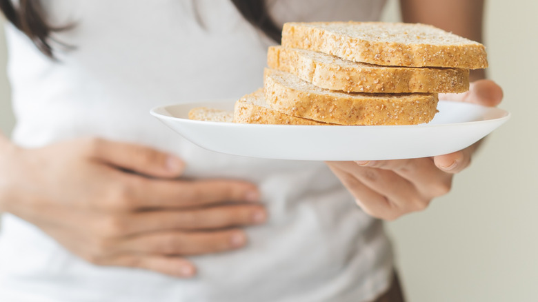 Een vrouw die haar buik aanraakt en een bord brood vasthoudt