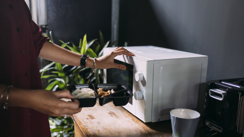 Vrouw die plastic afhaalcontainer in de magnetron zet