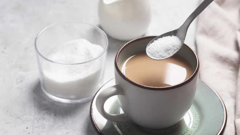 De hand van een vrouw die wat stevia aan haar koffie toevoegt