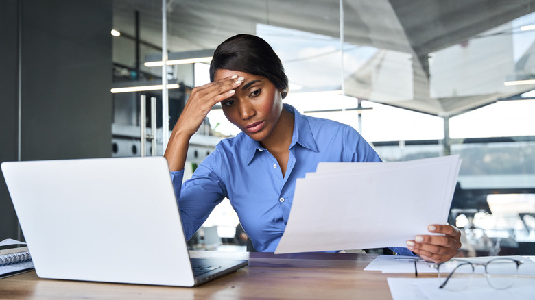 Een gestresste vrouw op het werk met haar tempel terwijl ze over papieren kijkt