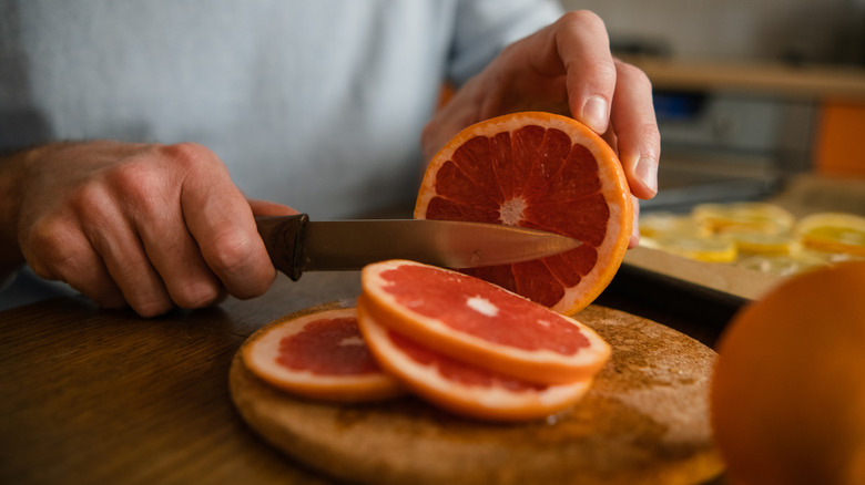 De handen van een man die rode grapefruit in kleine secties snijden