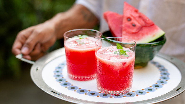 Twee glazen watermeloensap op een bord nabij een plakje watermeloen