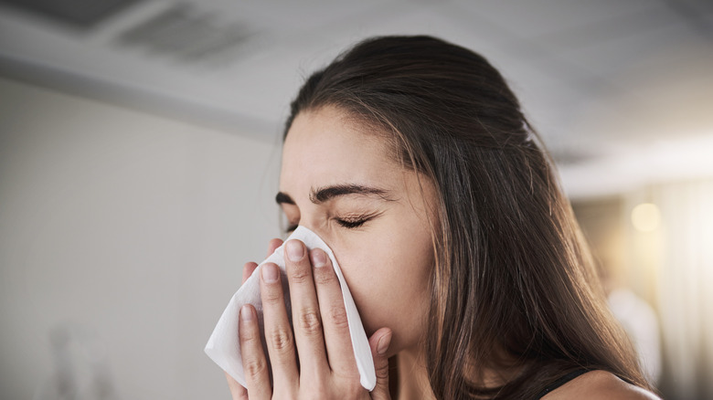 Jonge vrouw die haar neus in tissue blaast
