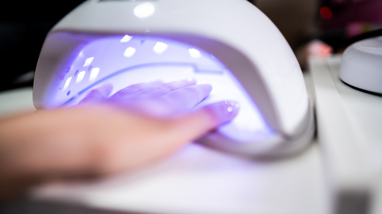 De hand van een vrouw met gel nagellak die drogen in een UV -lichtkamer