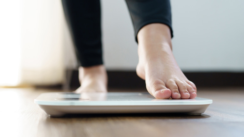 Vrouw die op schaal stapt om thuis naar gewicht te kijken
