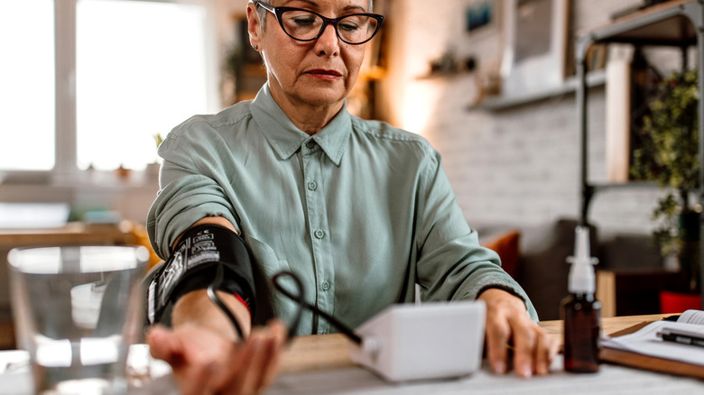 Vrouw die haar bloeddruk aan de keukentafel neemt