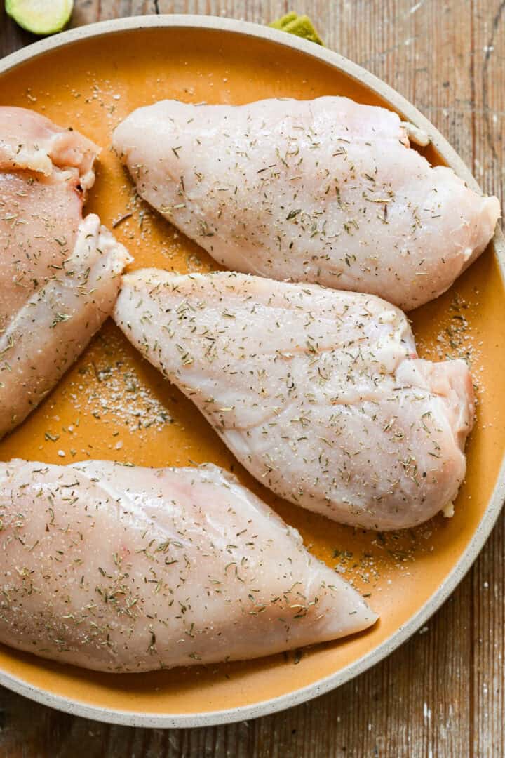 Rauwe kipfilets op een bord gekruid met zout, tijm en knoflookpoeder.