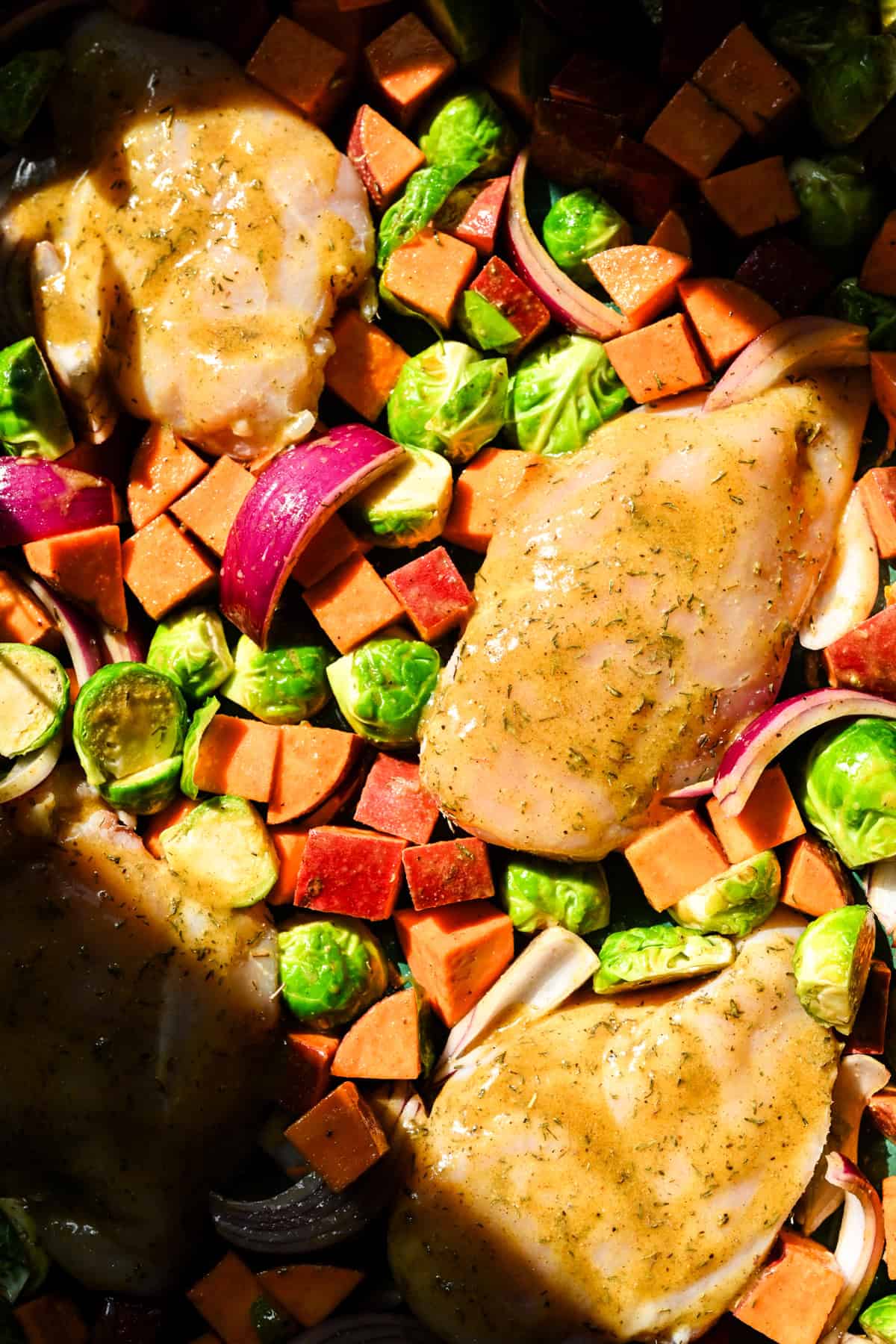 Overhead uitzicht op esdoorn mosterdplaat pan kip met herfstgroenten op een groene plaatpan voor het bakken.