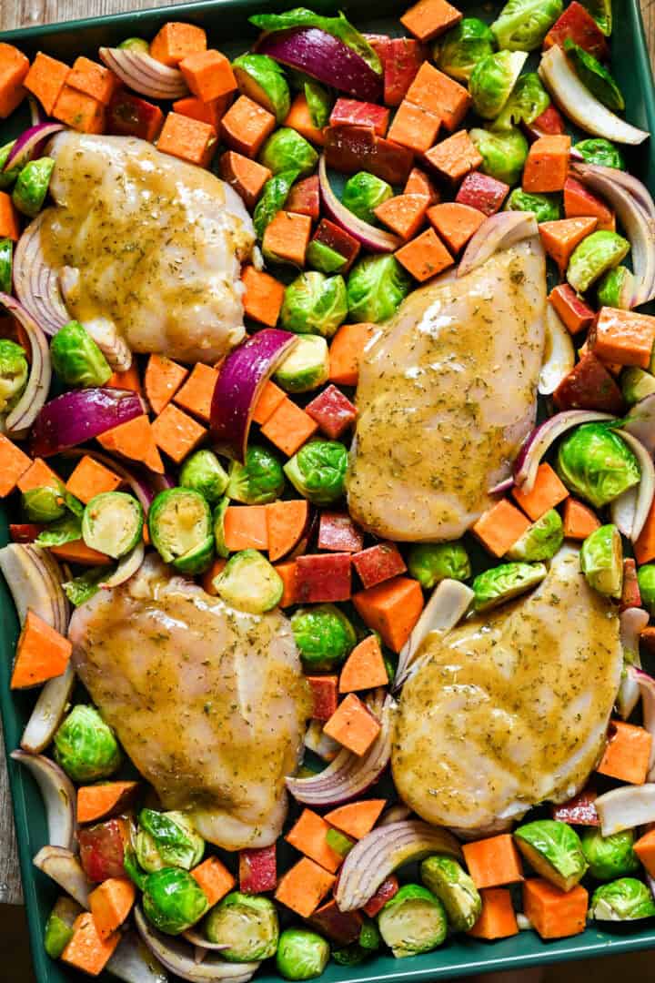 Overhead uitzicht op esdoorn mosterdplaat pan kip met herfstgroenten op een groene plaatpan voor het bakken.