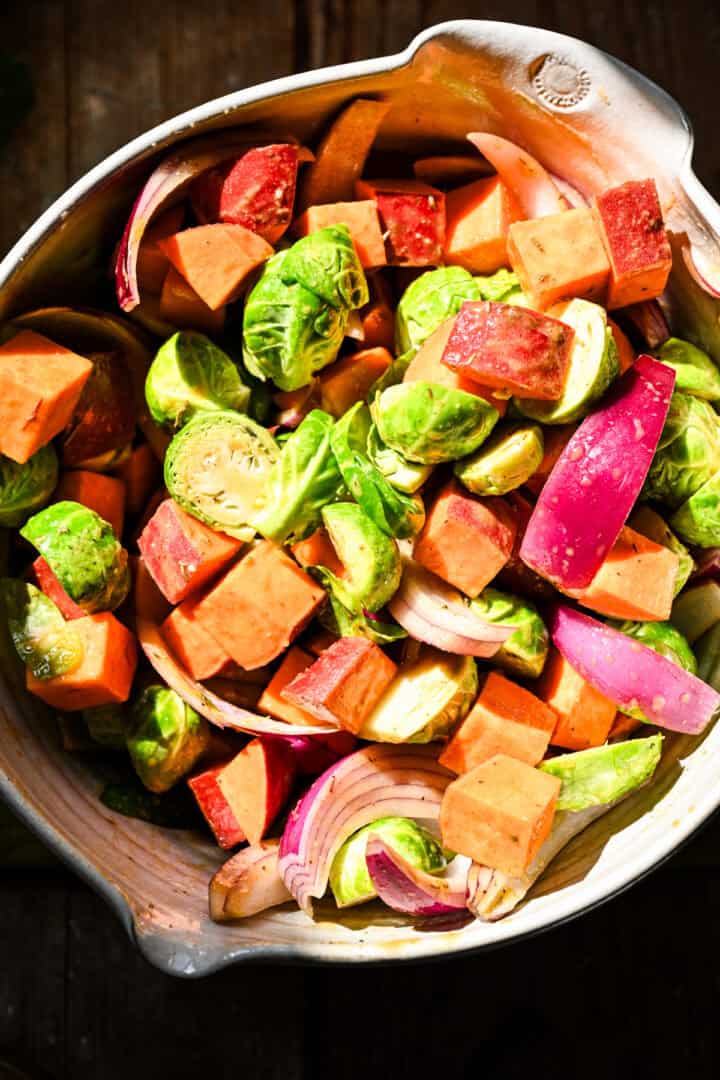 Rode ui, spruitjes en zoete aardappelen in een kom gegooid in esdoorn mosterddressing.