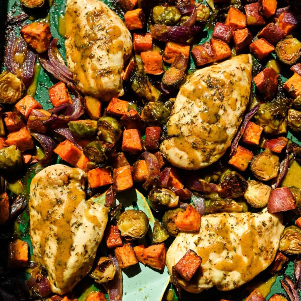 Overhead view of maple mustard sheet pan chicken with roasted fall vegetables on a green sheet pan.