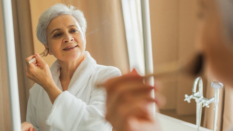 Rijpe vrouw die gezichtsmake -up in Mirror opdraagt