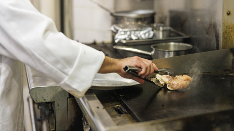 man die een tang in de commerciële keuken gebruikt om kip te koken