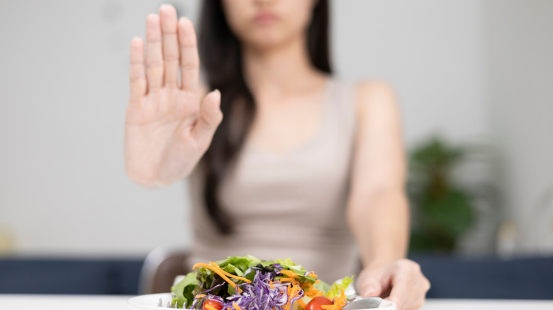 Een vrouw die een bord salade wegduwt