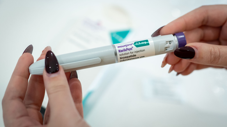 Twee handen met gelakte nagels die de Mounjaro-pen vasthouden.