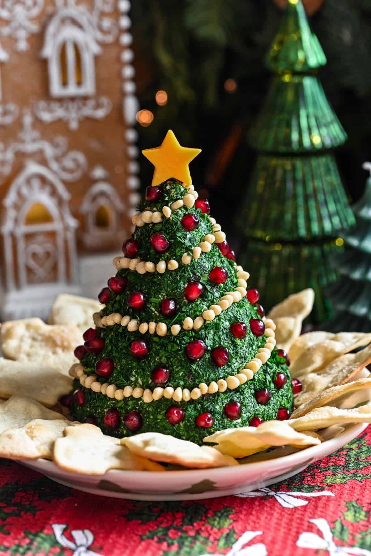 Kerstboomvormige kaasbal bedekt met kruiden en versierd met pijnboompittenslinger en granaatappelornamenten.