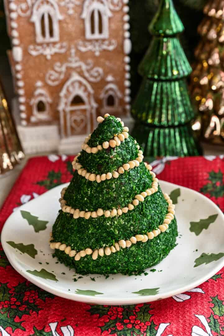Kerstboomvormige kaasbal bedekt met gehakte kruiden en versierd met pijnboompittenslinger.