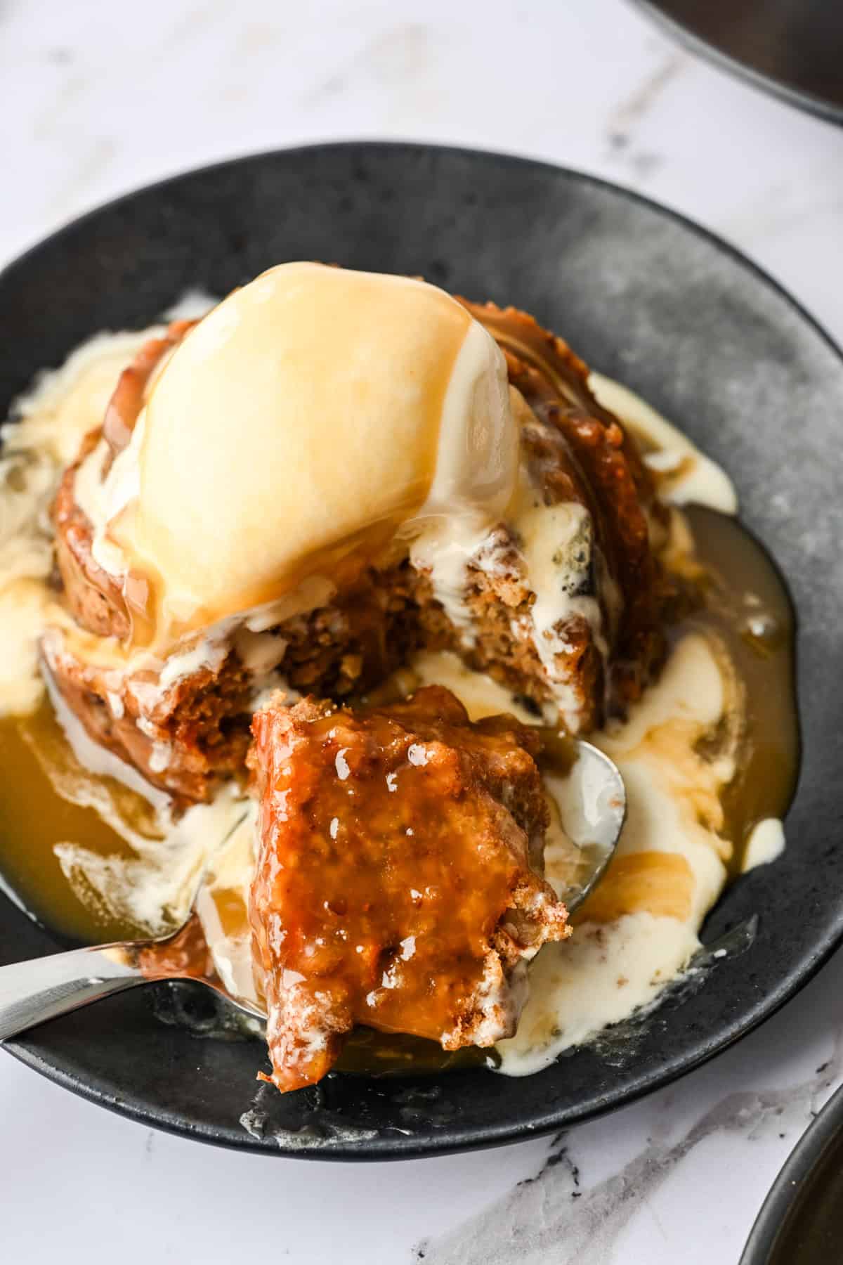 Close-up van figgy pudding met ijs en karamelsaus met een hapje eruit.