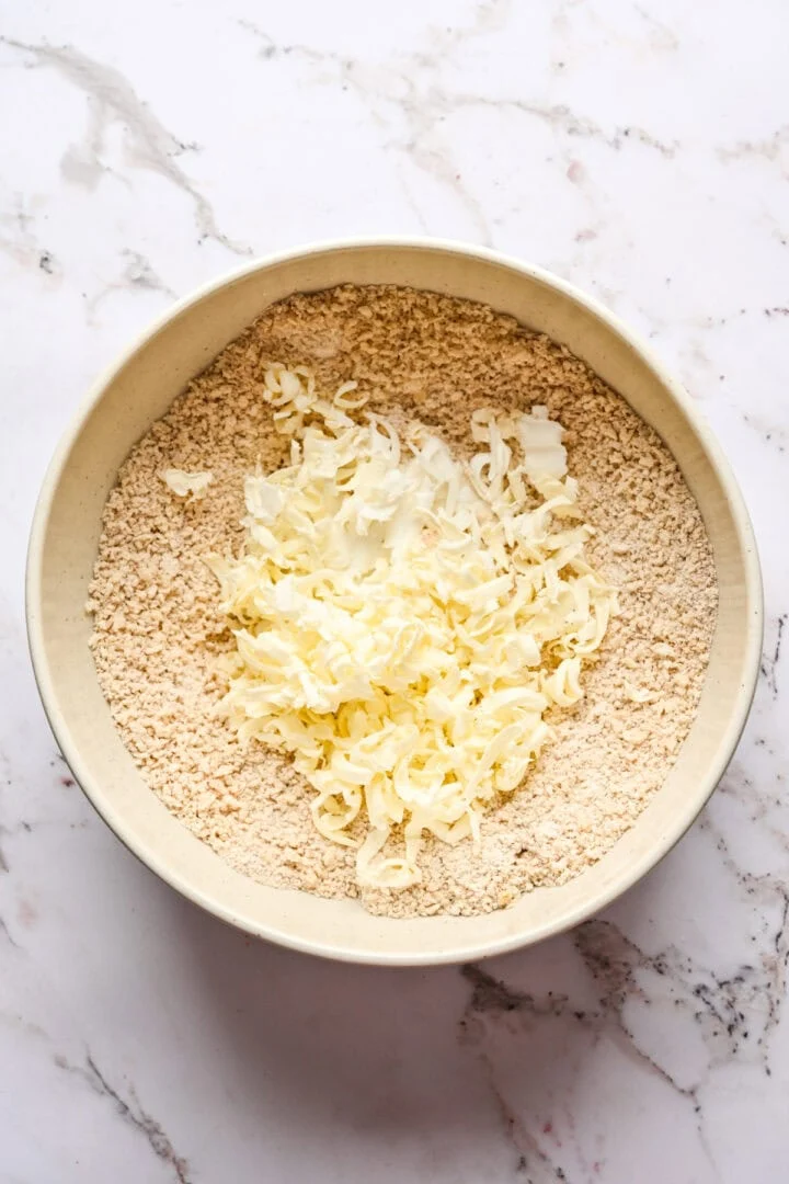 Droge ingrediënten van vijgenpudding, gegarneerd met geraspte bevroren boter en bakvet.