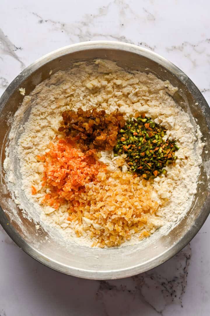 panettone koekjesdeeg in een kom met gehakte pistachenoten, gekonfijte sinaasappel en citroen en rozijnen.