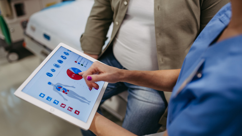 Een persoon in scrubs die naar een kaart op een iPad-scherm wijst naar een man op een brancard.