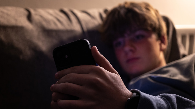 Een jonge jongen die een telefoon vasthoudt en zijn hoofd tegen een bank laat rusten.
