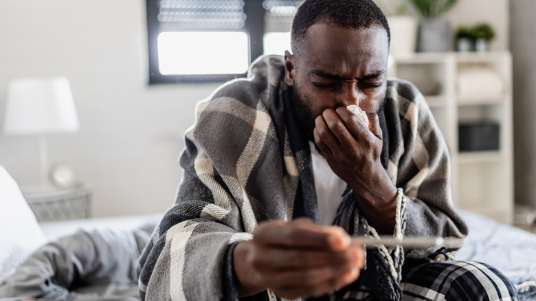 man ziek in de slaapkamer terwijl hij de thermometer controleert