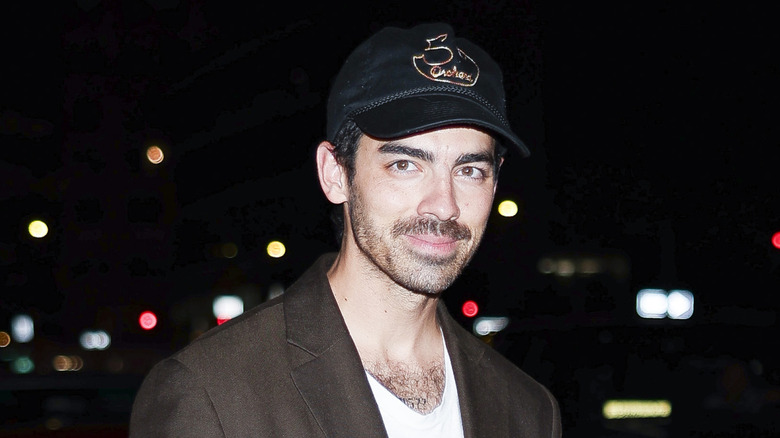 Joe Jonas in het donker met een baseballpet op en een grijnzende glimlach.