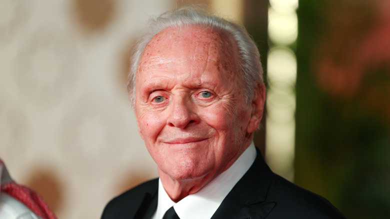 Anthony Hopkins in pak en stropdas glimlachend met een onscherpe achtergrond.