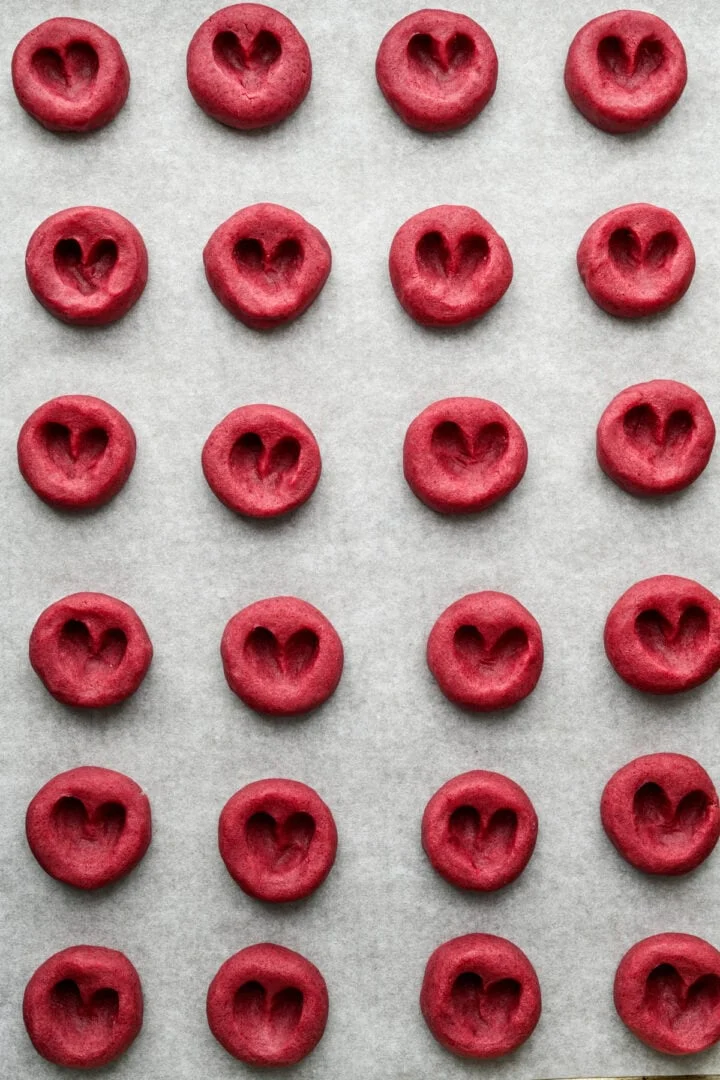 Frambozenhart-vingerafdrukkoekjes op bakplaat voordat ze worden gevuld met jam.