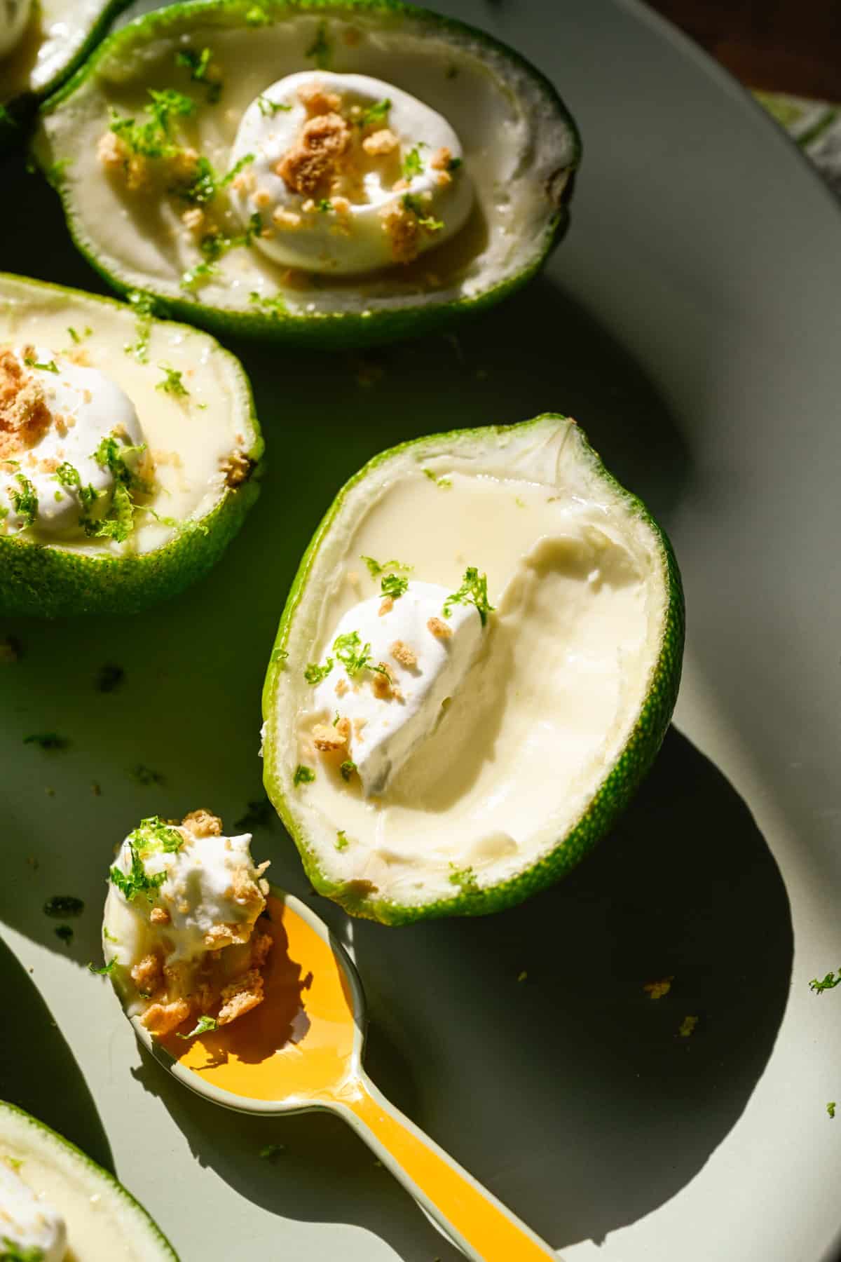 Close-up van limoen posset gegarneerd met slagroom en graham cracker kruimels op lichtgroen bord met een lepel eruit gehaald.