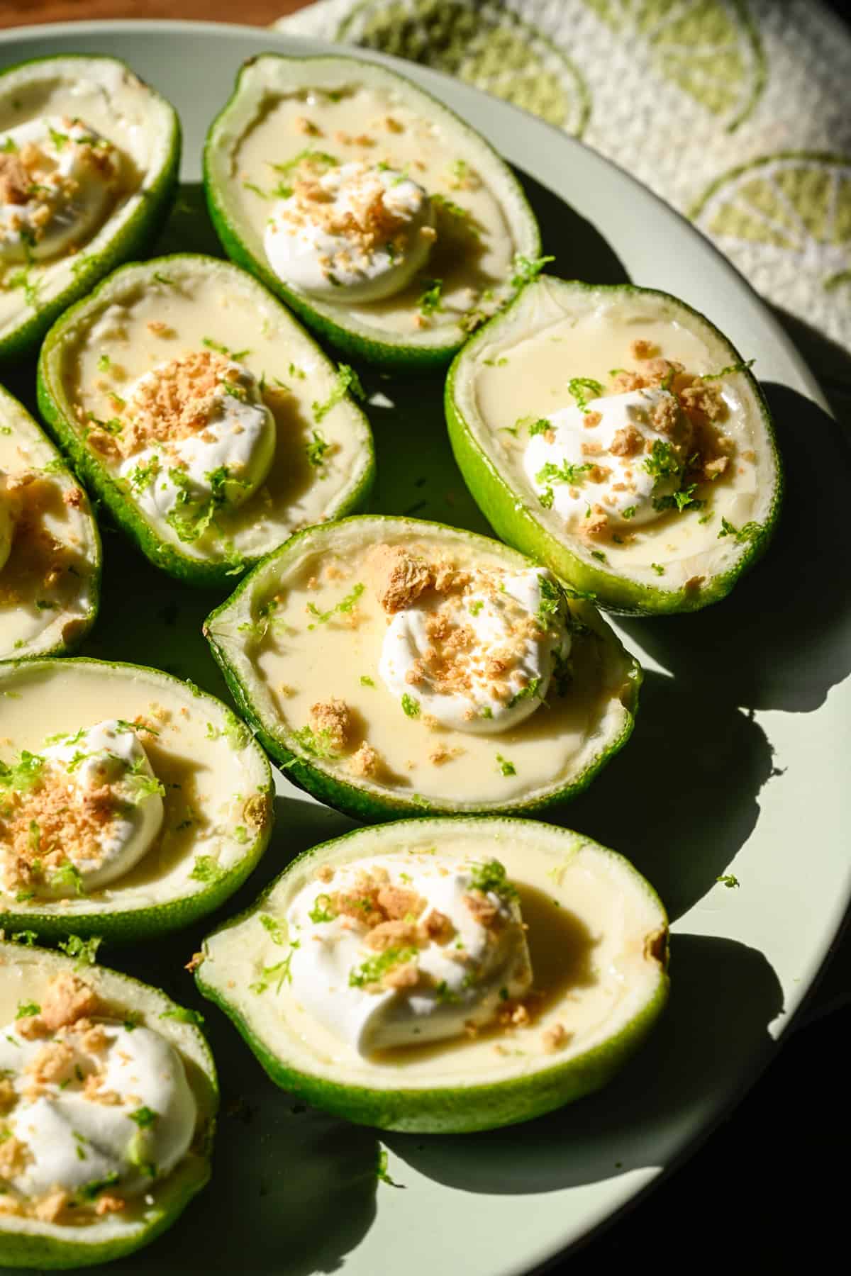 Close-up van limoenpossets gegarneerd met slagroom en graham crackerkruimels op lichtgroene plaat. 