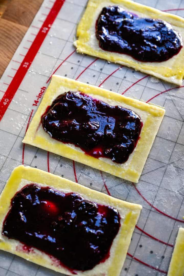 rechthoek van pop-tartdeeg, gegarneerd met bosbessenvulling en eierwas langs de randen.