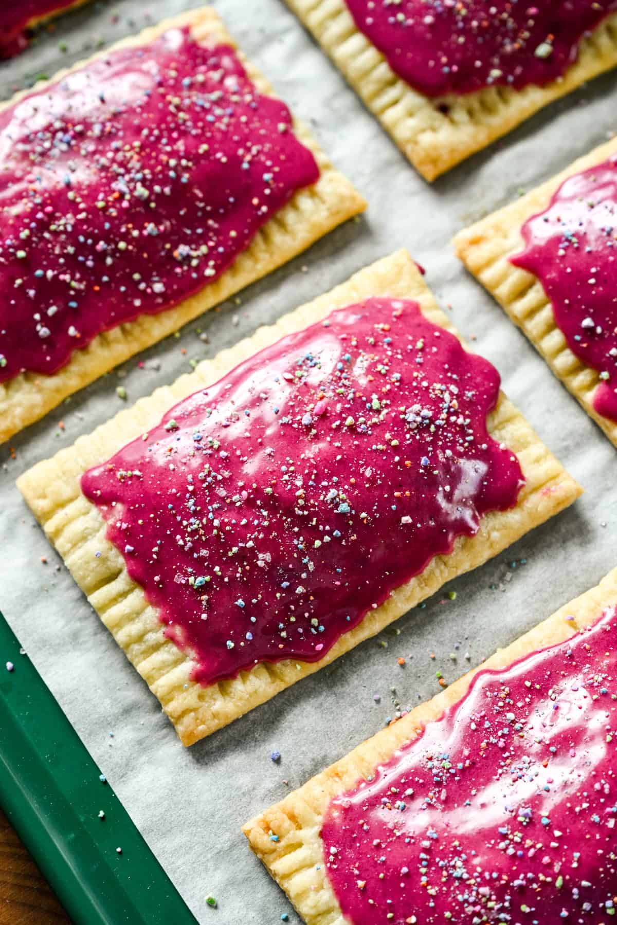 close-up van zelfgemaakte bosbessenpop-tarts met felroze glazuur en hagelslag op een bladpan.