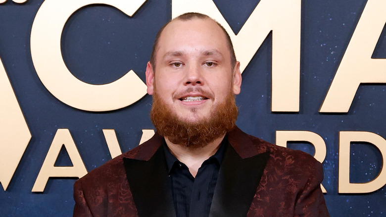 Luke Combs in een rode colbert voor het ACMA Awards-logo