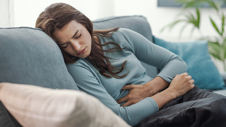 Een jonge vrouw op de bank die lijdt aan menstruatiepijn.