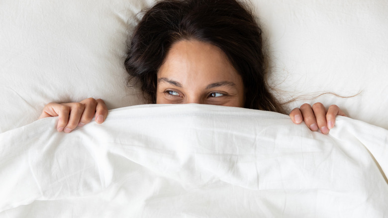 Vrouw die lacht terwijl ze zich verstopt onder haar dekbed