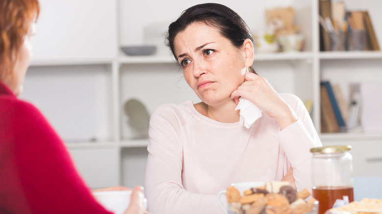 Vrouw zit aan een tafel en houdt een papieren servet vast