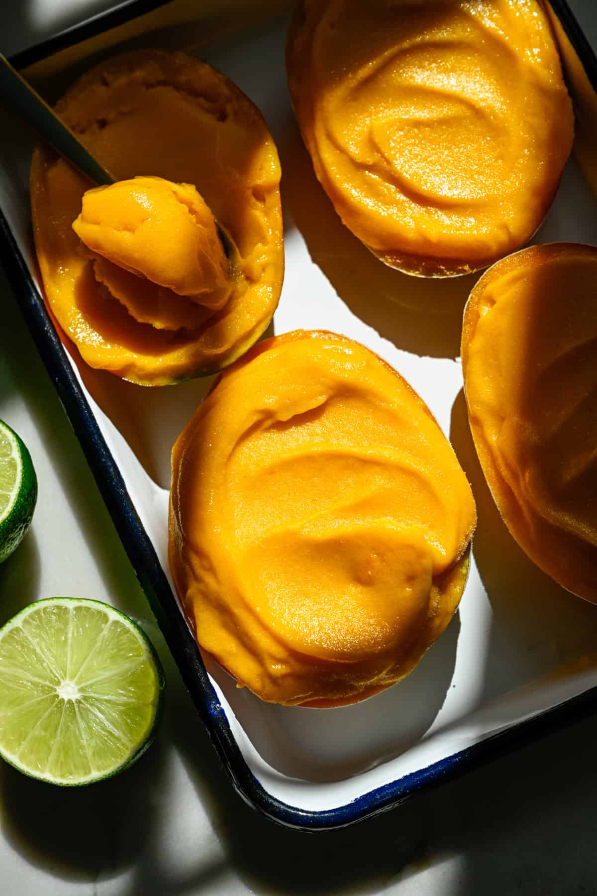 Bovenaanzicht van mangosorbet in een mangohelft op een bakplaat met een paar andere.