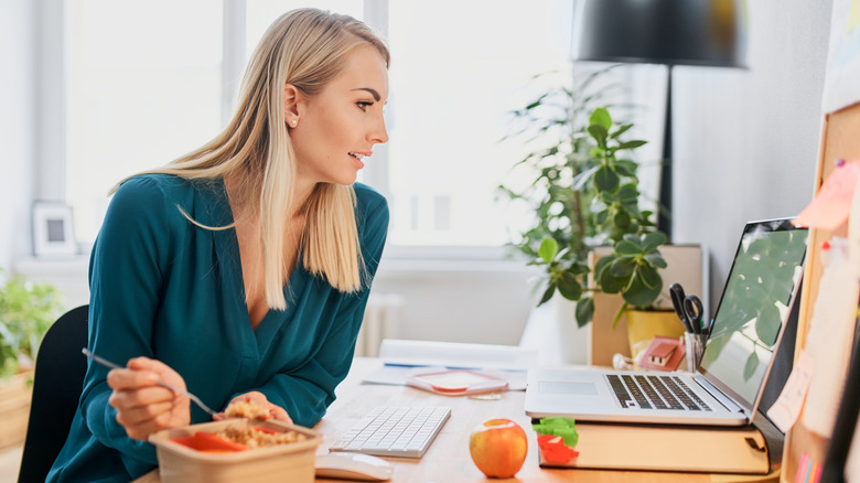 Vrouw kijkt naar haar laptop terwijl ze eet