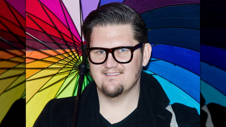 Jay McCarroll glimlacht terwijl hij een regenboogparaplu vasthoudt