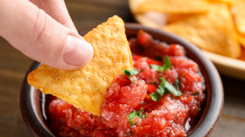 Persoon die nachochip in pittige salsasaus dompelt aan tafel