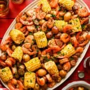 Bovenaanzicht van garnalen op bladpan koken op een schotel met maïs, garnalen, worst en aardappelen.