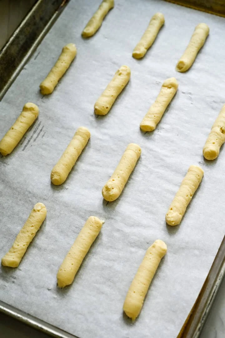 Milano-koekjesdeeg in rechte lijnen op een bakplaat gelegd.