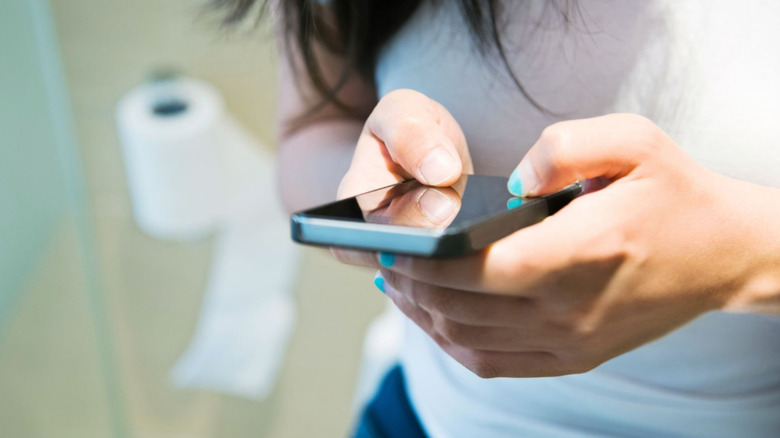 vrouwen die haar mobiele telefoon gebruiken in het toilet