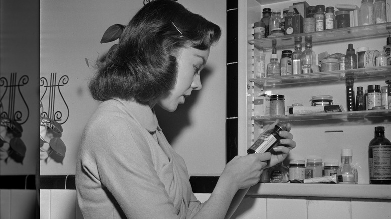 vrouw in de jaren vijftig die naar producten in het medicijnkastje kijkt