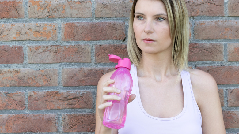 vrouw met een herbruikbare waterfles die buiten tegen een bakstenen muur staat