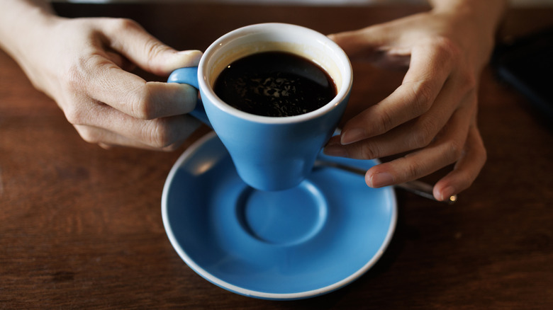 Persoon die een keramische kop koffie vasthoudt terwijl hij aan een tafel zit