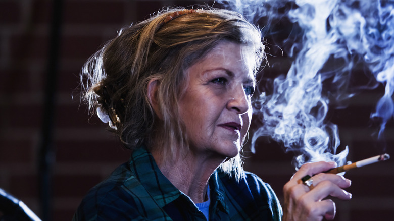 Een vrouw van in de zestig die een sigaret rookt in een donkere kamer
