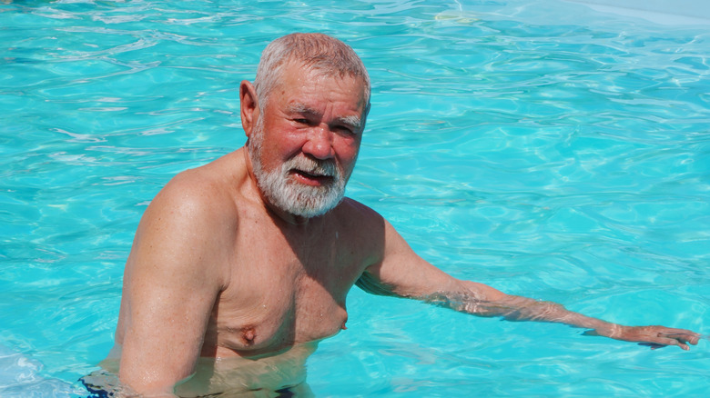 Senior man met een bruine huid die lacht terwijl hij in een zwembad staat